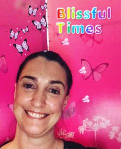 Woman grinning forward with a pink backdrop with butterflies on it and the words 'Blissful Times'.