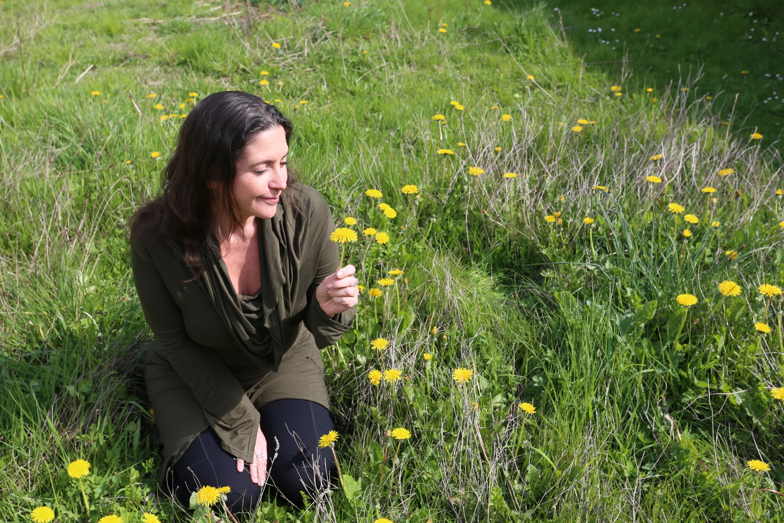 Woman kneeling in a field amongst yellow flowers holding one of them in her hand.